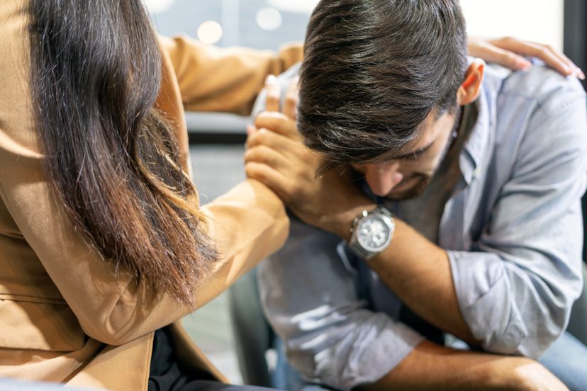 A wife consoling her husband by placing her hands on his shoulders