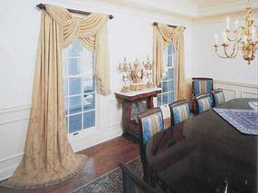 © A formal dining room drapery uses classic damask fabric to cross-tie in a swagged valance before falling off to a shorter length at one side.