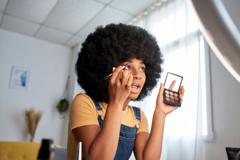 Afro woman holding a make-up palette while painting her eyebrows. Make-up and beauty concept.