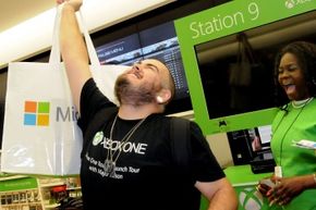 The first consumer to buy an Xbox One at the midnight release event at the Florida Mall in Orlando, Fla. raises his purchase triumphantly in the air.  