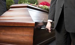 A person holds the handle of a wooden casket.