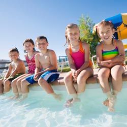 two boys and three girls sitting on the side of a pool