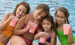 four girls drinking smoothies while sitting by a pool