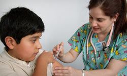A nurse administers a vaccination, like MMR, in the shoulder muscle of a young boy.