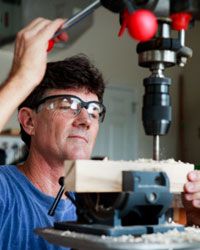 A man wears safety glasses as he drills into a piece of wood.