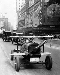 A car with wings and a propeller protruding from the radiator grille drives through Times Square, New York. The invention of A.H. Russell of Nutley, New Jersey.