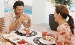 Mature Couple Sit Face-to-Face Over Breakfast at a Patio Table Laughing