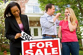 Couple celebrating buying a house while their realtor puts up a sold sign.