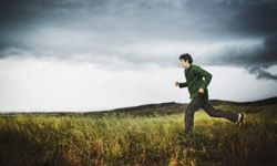 man running in field, ominous sky in background