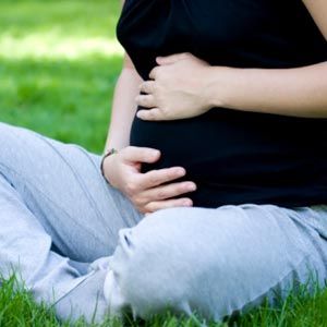 pregnant Caucasian woman sitting in grass holding her belly