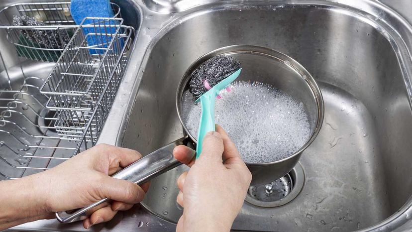 Person washing an aluminum pot with cream of tartar and soap.