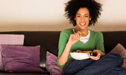 woman watching TV, sitting on couch eating snacks