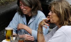8月6日，在伦敦市中心，两名女子一边喝酒一边抽烟。＂border=