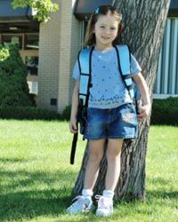 kindergarten-age girl standing next to tree getting her photograph taken on first day of school