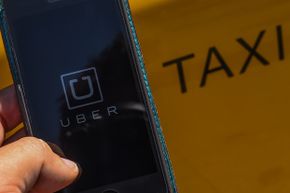 智能手机应用程序“ Uber”徽标显示在西班牙巴塞罗那的出租车旁边的手机上。“width=