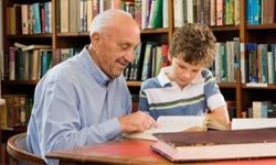 caucasian male senior citizen reading with caucasian male boy in library