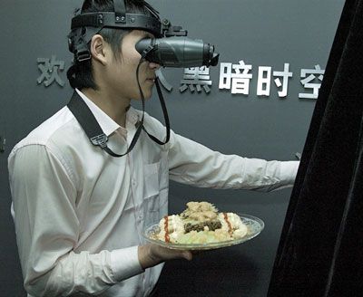 A waiter wearing night-vision goggles carries food into a dark restaurant in Beijing, China. 
