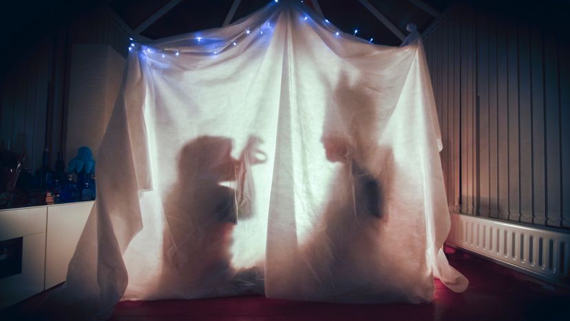 A parent and a child inside a lit up tent in a dark room. 