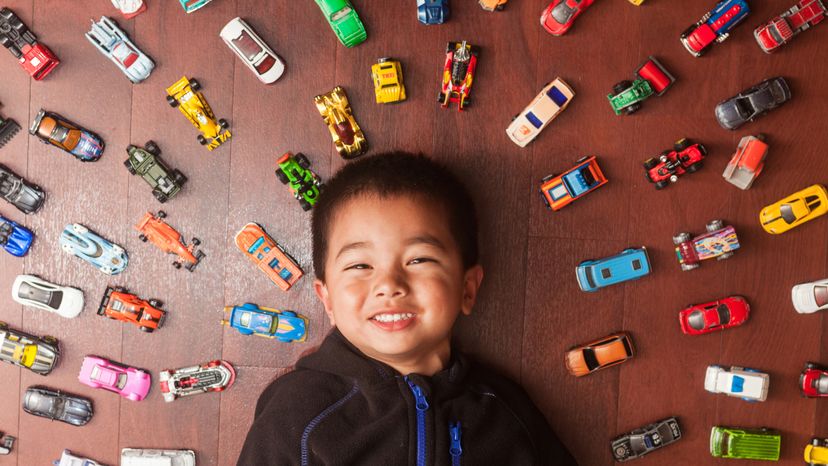 A little boy laying on the floor surrounded by toy cars. 